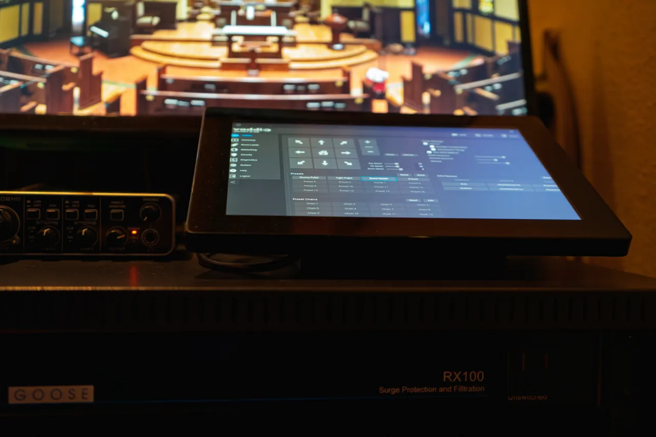 Touchscreen control surface for the audio mixing system at the front-of-house position, with a monitor showing the sanctuary behind it.