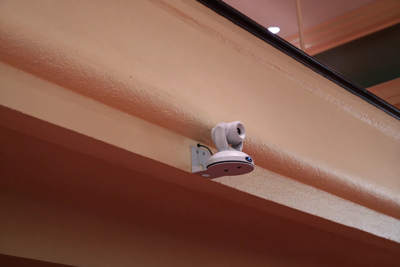 A balcony-mounted PTZ camera against the sanctuary painted beams.