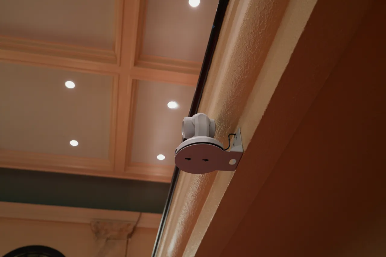 A white PTZ camera mounted beneath the sanctuary coffered ceiling.