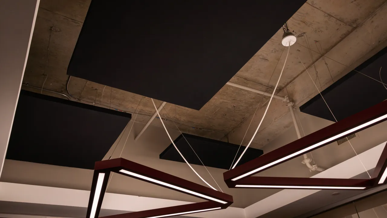 Suspended acoustic panels and pendant light fixtures across the exposed-concrete ceiling.