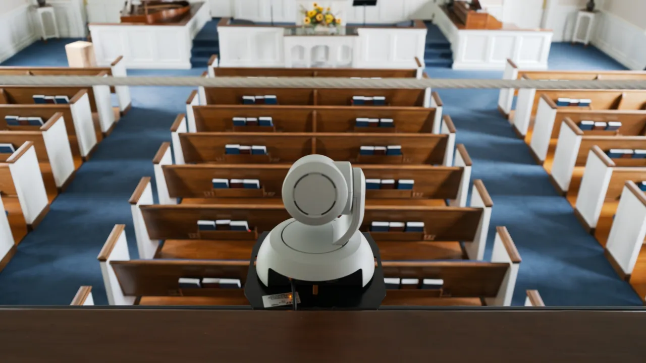 A PTZ camera mounted on the balcony rail, overlooking the pews below.