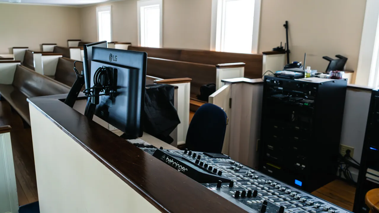 Reverse view of the sound booth showing a monitor, mixing console, and the equipment rack behind the seating.