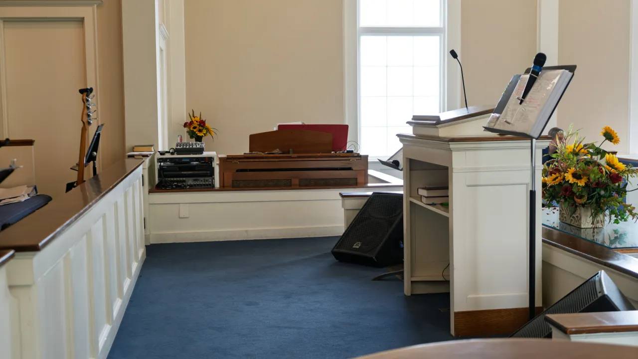 View toward the rear of the sanctuary showing pews, the balcony, and a ceiling-mounted projector.