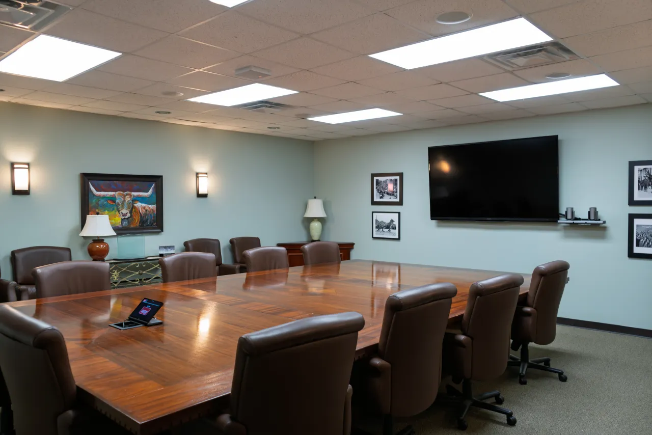 A conference room with a wall-mounted display, leather seating, and a tabletop control panel.