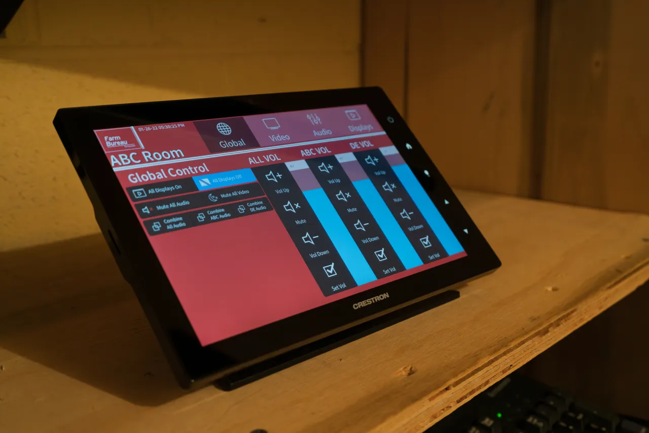 A Crestron touchscreen control panel displaying the room audio and video controls.